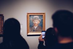 a man taking a photo of a painting on the wall with his cell phone in front of him