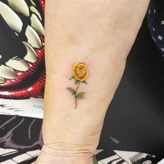 a small yellow rose tattoo on the left inner forearm and wrist area, with green leaves