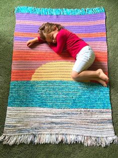 a woman laying on top of a multi colored knitted area rug with fringes