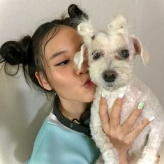 a woman holding a small white dog in her arms and kissing it's face