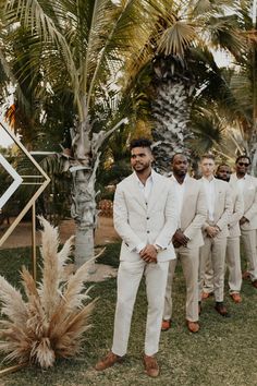 a group of men standing next to each other in front of palm trees and grass