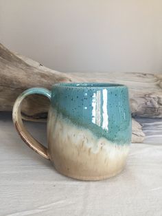 a blue and white coffee mug sitting on top of a wooden table next to driftwood