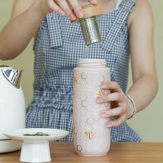 a woman pouring tea into a pink cup on top of a wooden table next to a white plate