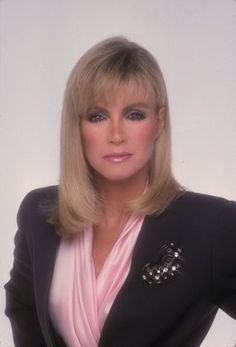 a woman with blonde hair wearing a black jacket and pink scarf posing for a photo