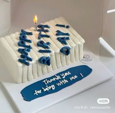 a white cake with blue frosting and a lit candle on top that says happy birthday