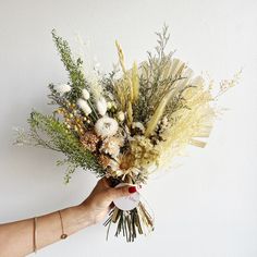 a person holding a bunch of flowers in their hand on a white wall behind them