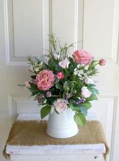 a white vase filled with pink flowers on top of a table