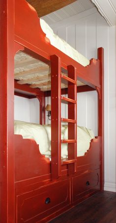 a red bunk bed with white sheets and ladders