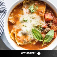 a white bowl filled with pasta and meat covered in sauce, garnished with fresh herbs