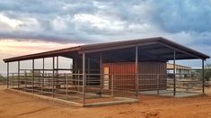 a small metal building sitting in the middle of a dirt field under a cloudy sky