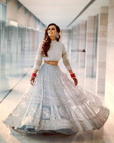 a woman in a white and blue lehenga is posing for the camera with her hands on her hips