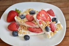 some strawberries and blueberries are on a white plate with granola toppings