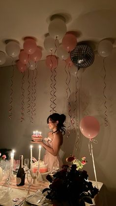 a woman standing in front of a table with candles and balloons on the wall behind her