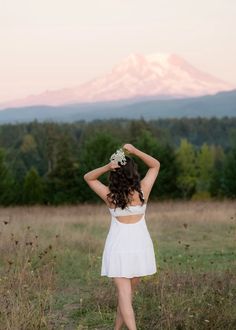 a woman in a white dress walking through a field with her back to the camera