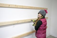 a woman in a pink vest holding a drill and looking at the wall behind her