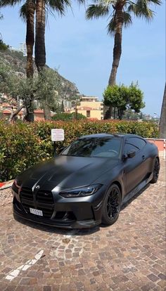 a black sports car parked in front of palm trees on a cobblestone driveway