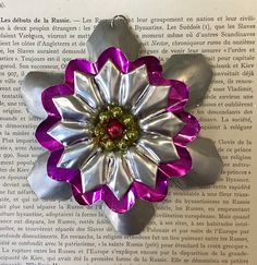 a silver and purple flower brooch sitting on top of a piece of book paper