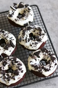 six chocolate donuts with white frosting and oreo pieces on a cooling rack