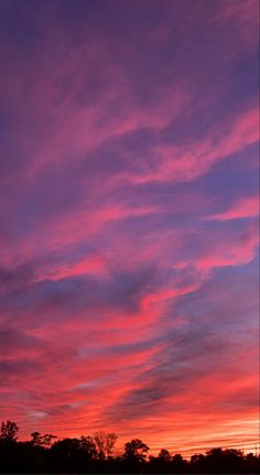 the sky is pink and purple as the sun sets in the distance with trees behind it