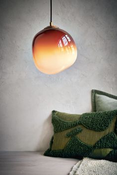 a lamp hanging over a bed next to a green pillow and throw pillows on the floor