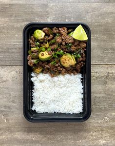 a tray with rice, meat and vegetables on it next to a lime wedge in the middle