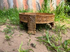 a wooden bowl sitting on top of a dirt ground next to green grass and weeds