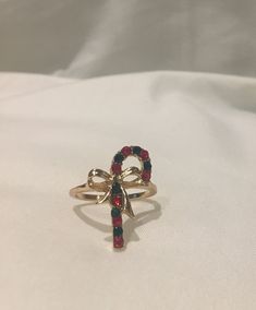 a gold ring with red, blue and green beads on the side sitting on a white cloth