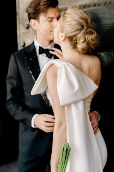 a man in a tuxedo kissing a woman in a white dress with green flowers