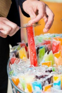 a man is cutting into a colorful cake with a red candle in the middle and gummy bars around it