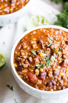 two white bowls filled with chili, beans and avocado garnished with cilantro