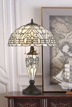 a table lamp sitting on top of a wooden dresser next to a framed photo and painting