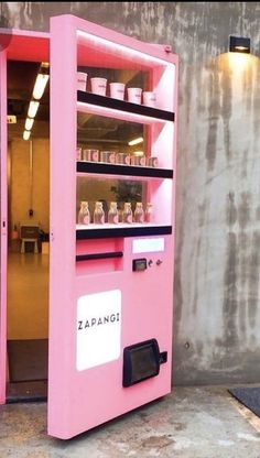 a pink vending machine sitting on top of a cement floor next to a wall