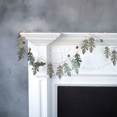 a white mantle with garland and lights on it in front of a gray wall behind the fireplace