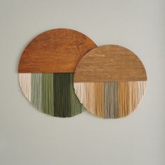 two circular wooden plates with different colored fringes on each one, hanging from the wall