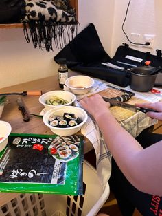 a person sitting at a table with bowls of sushi and chopsticks on it