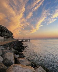 the sun is setting over the water and some rocks are in front of an apartment building