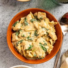 an orange bowl filled with pasta and spinach on top of a marble countertop