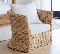 a wicker chair with white pillows in front of a bed