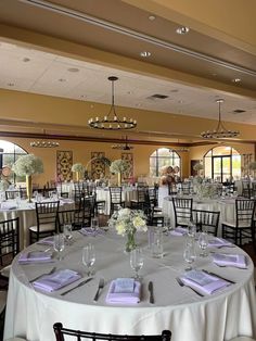 the tables are set up for a wedding reception with purple napkins and white flowers