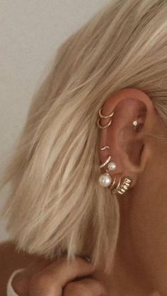 a woman with blonde hair wearing gold ear cuffs and pearled earrings in front of her face