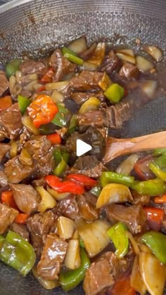 beef and peppers cooking in a wok with a wooden spatula on the side