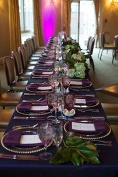 the long table is set with purple and white place settings for an elegant dinner party