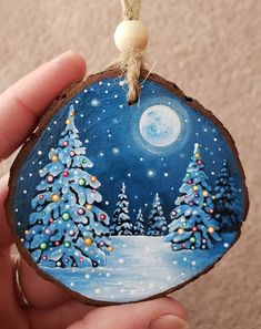 a hand holding a painted ornament with trees and snow in the night sky