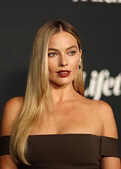 a woman with long blonde hair wearing a brown dress and red lipstick on her lips