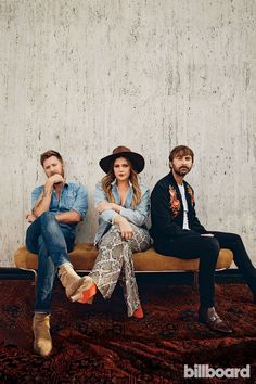 three people sitting on a bench in front of a wall