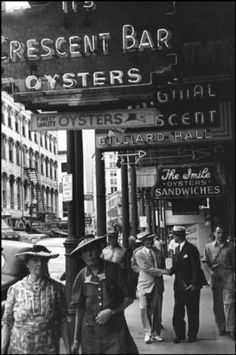 an old black and white photo of people walking on the sidewalk in front of a restaurant