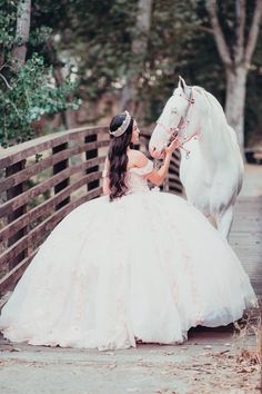 a woman in a wedding dress sitting on a bridge next to a white horse