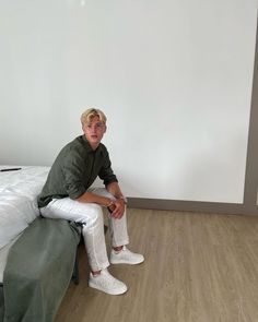 a man sitting on top of a bed next to a white wall and wooden floor