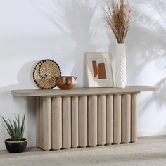 a wooden table topped with a vase next to a potted plant and framed pictures