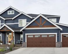 a blue house with two garage doors and brown trim on the front door is shown